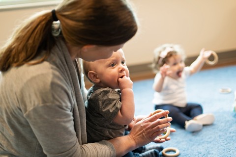 Childcare worker sits with inquisitive toddler